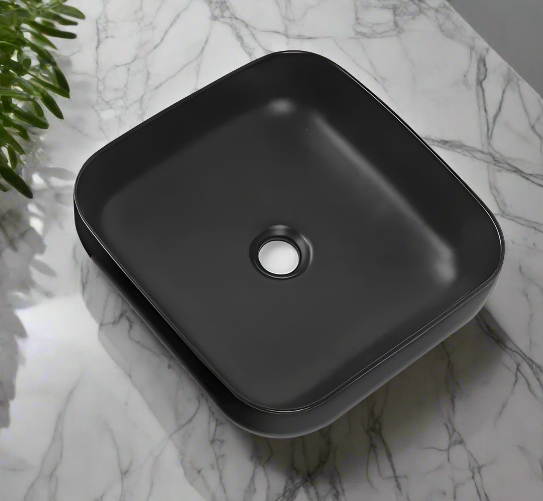 A sleek square-shaped matt black ceramic wash basin placed on a marble surface.