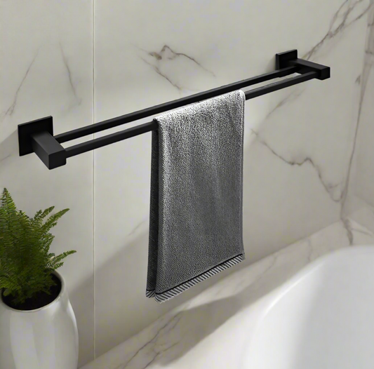 A black square double towel rail rack mounted on a white wall with a gray towel hanging on it, and a plant to the left.