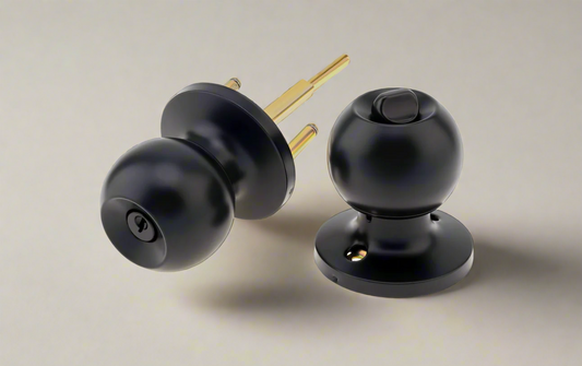 A set of two ball door knobs with a matte black finish and a metallic spindle behind them, placed against a light background.