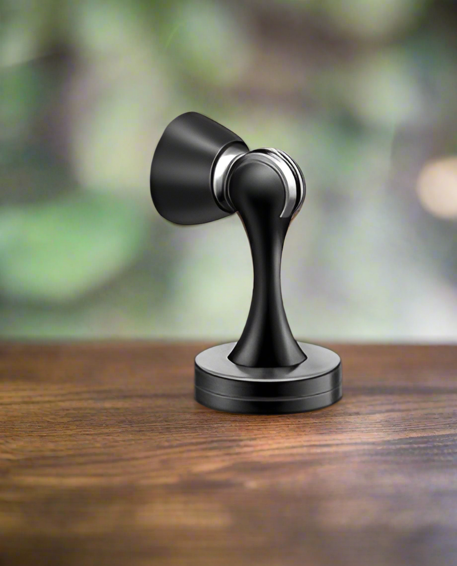 A black stainless steel door stopper with a matte finish, positioned on a wooden floor.