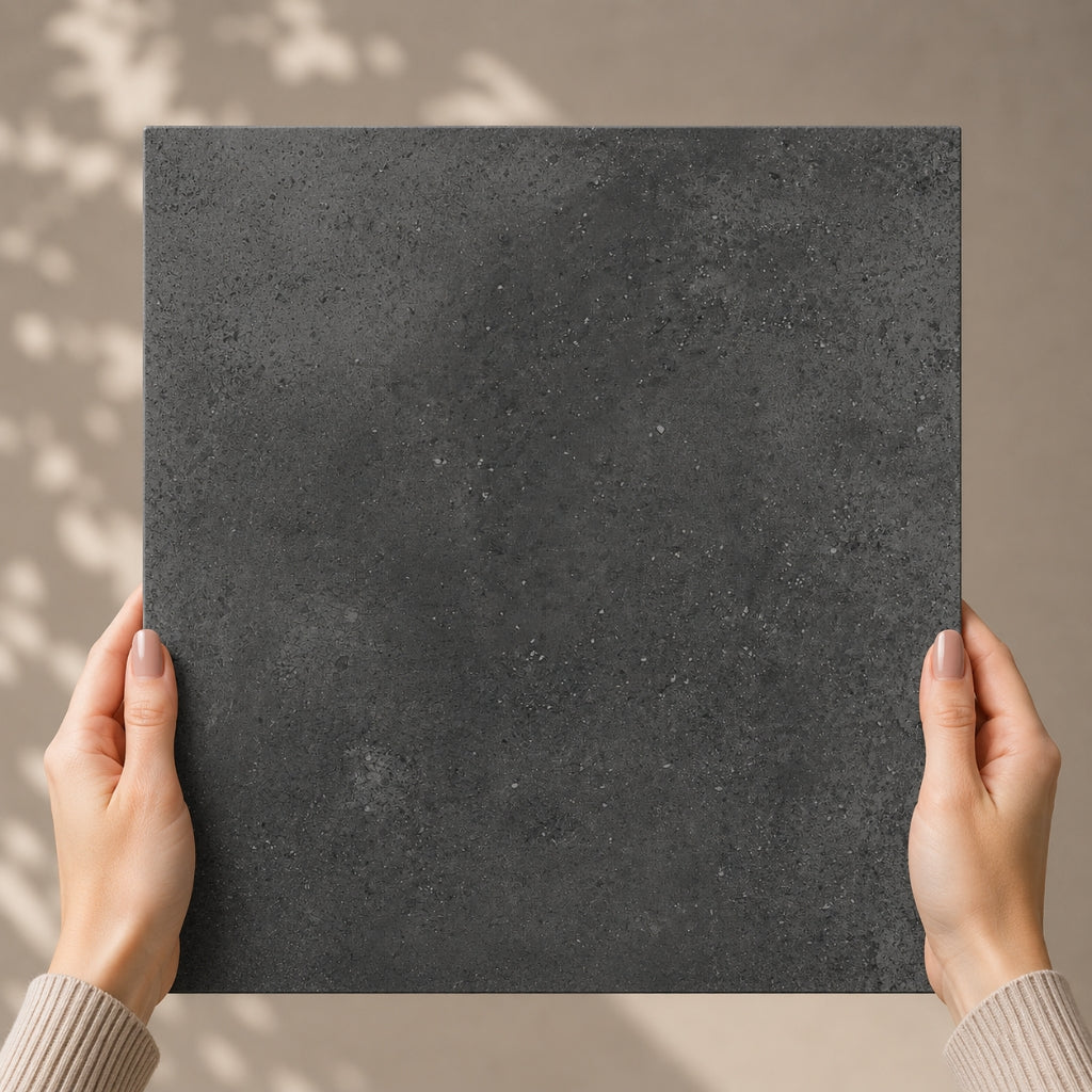 Person holding a square dark gray tile against a beige background