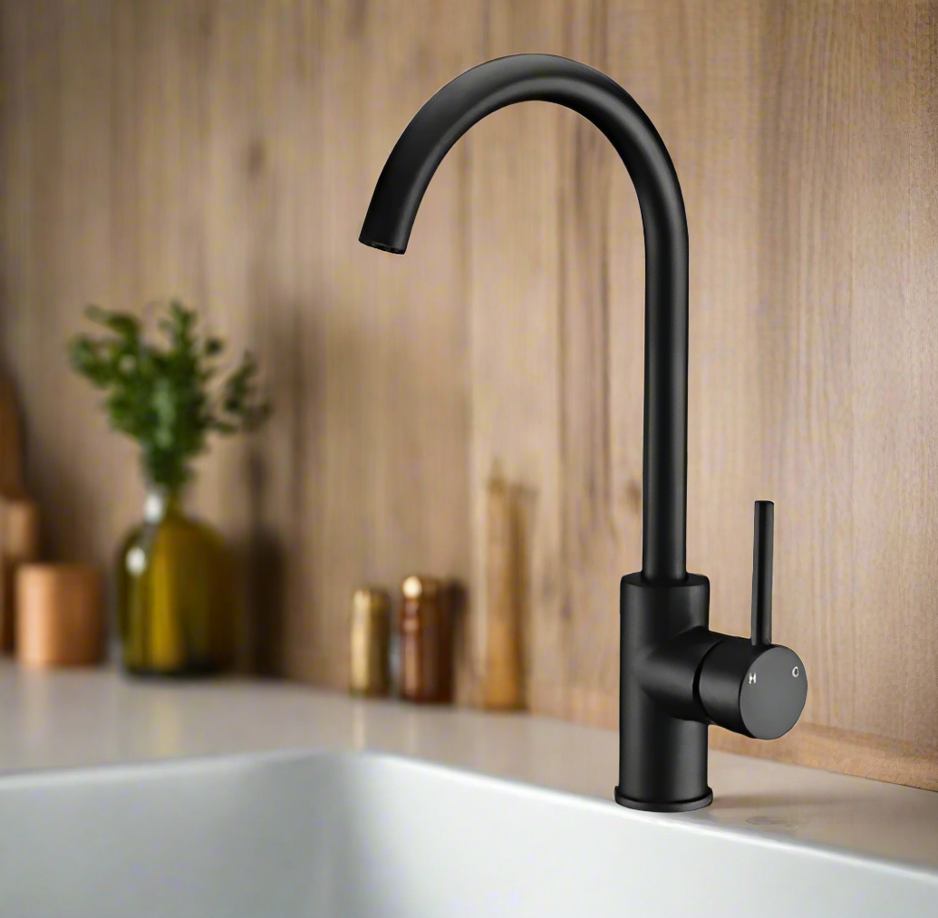 A modern black sink mixer tap with a curved top and smooth, rounded edges, installed on a white sink with a wooden backdrop.