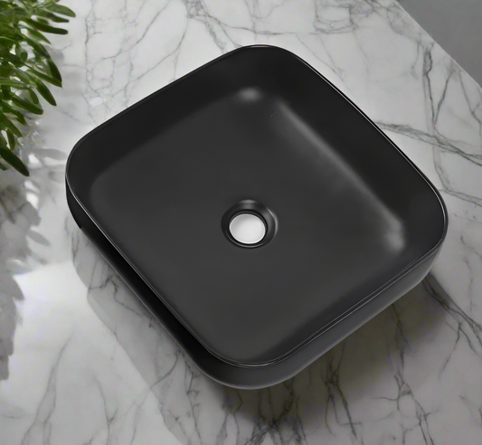 A sleek square-shaped matt black ceramic wash basin placed on a marble surface.