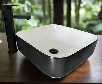 A modern ceramic square wash basin with a matte black exterior and white interior, displayed in a bathroom setting 