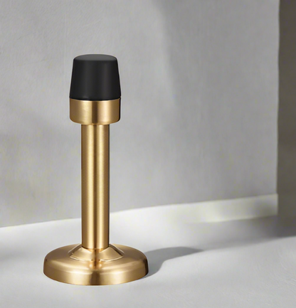 A black and silver wall-mounted door stopper with a rubber tip, installed on a wooden floor.