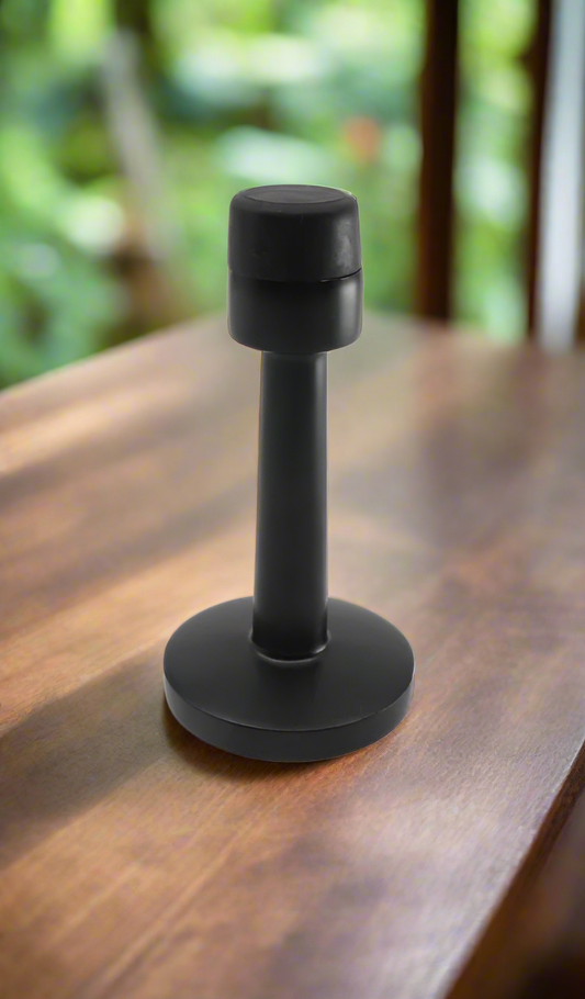 A black and silver wall-mounted door stopper with a rubber tip, installed on a wooden floor.