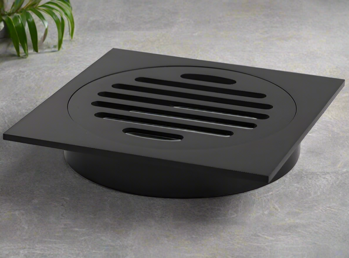 A black square floor waste drain grate installed on a tiled bathroom floor.
