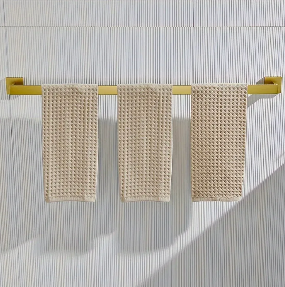 Three beige textured towels hanging on a gold towel rack against a striped wall.
