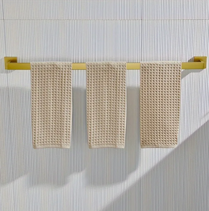 Three beige textured towels hanging on a gold towel rack against a striped wall.