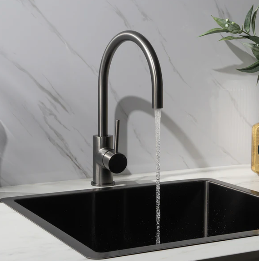 Modern kitchen faucet with running water over a black sink against a marble wall.