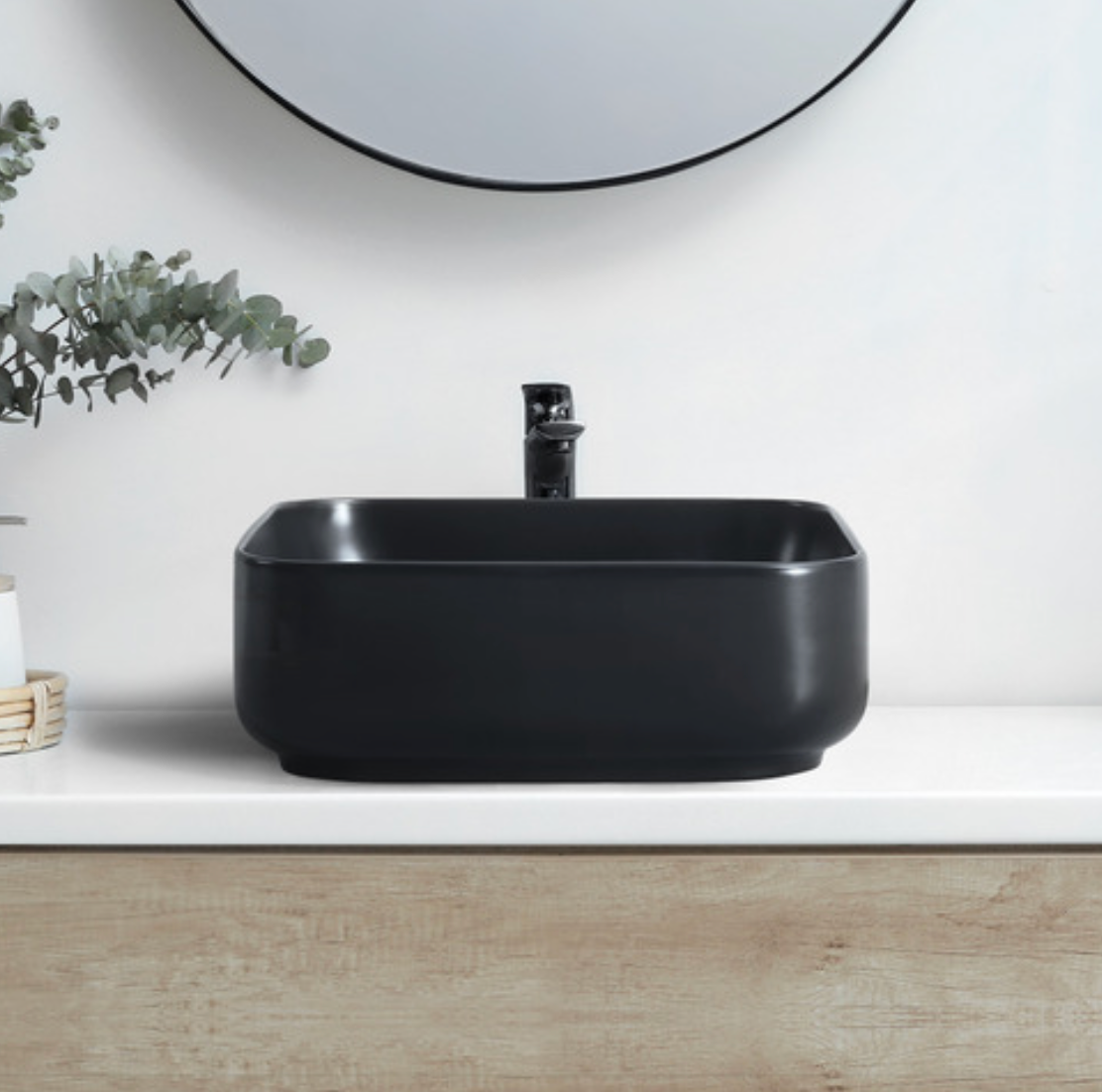 Black rectangular sink on a white countertop with a mirror and plant in the background