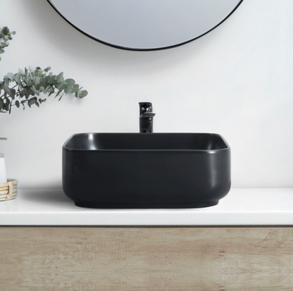 Black rectangular sink on a white countertop with a mirror and plant in the background