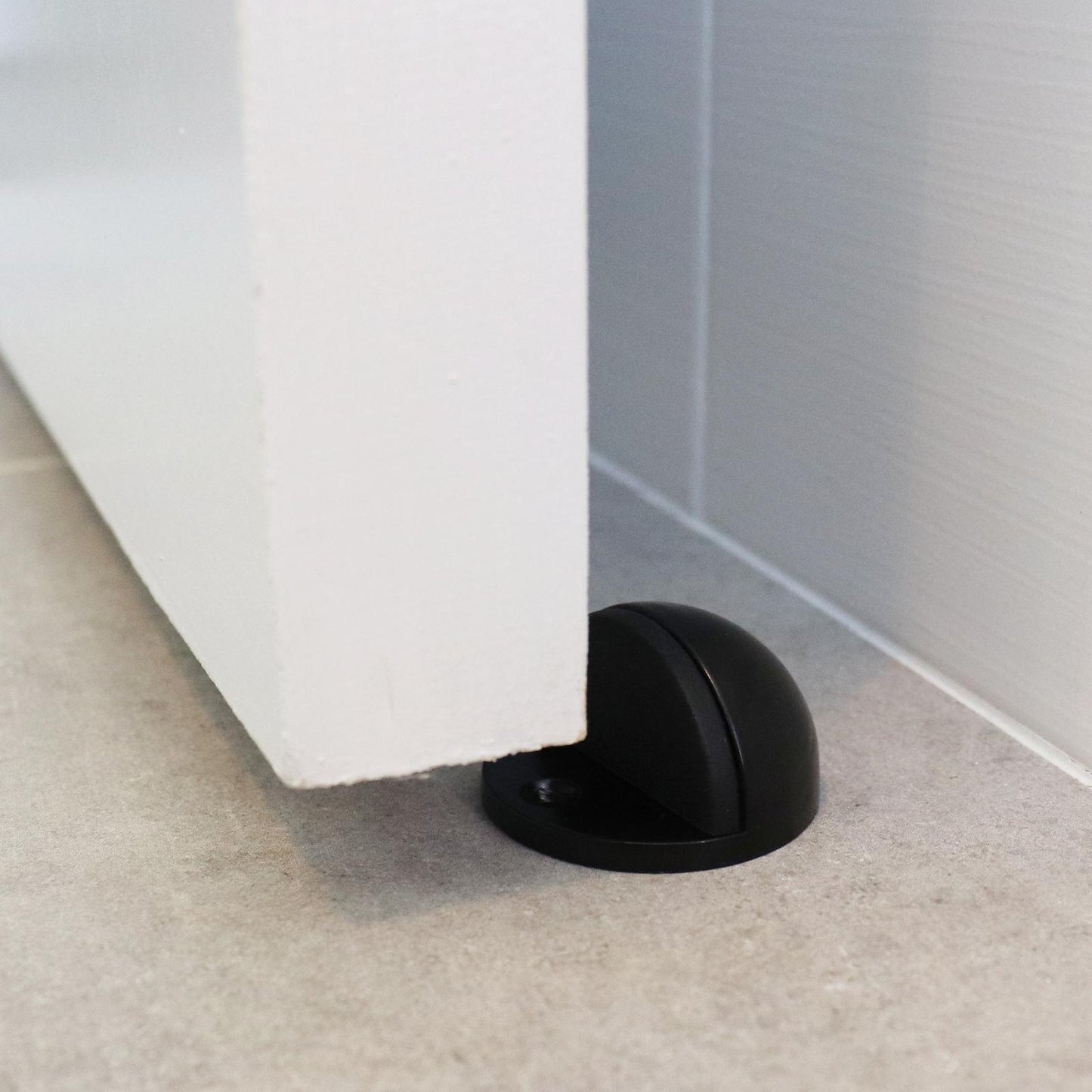 Black door stopper on a carpeted floor next to a white door