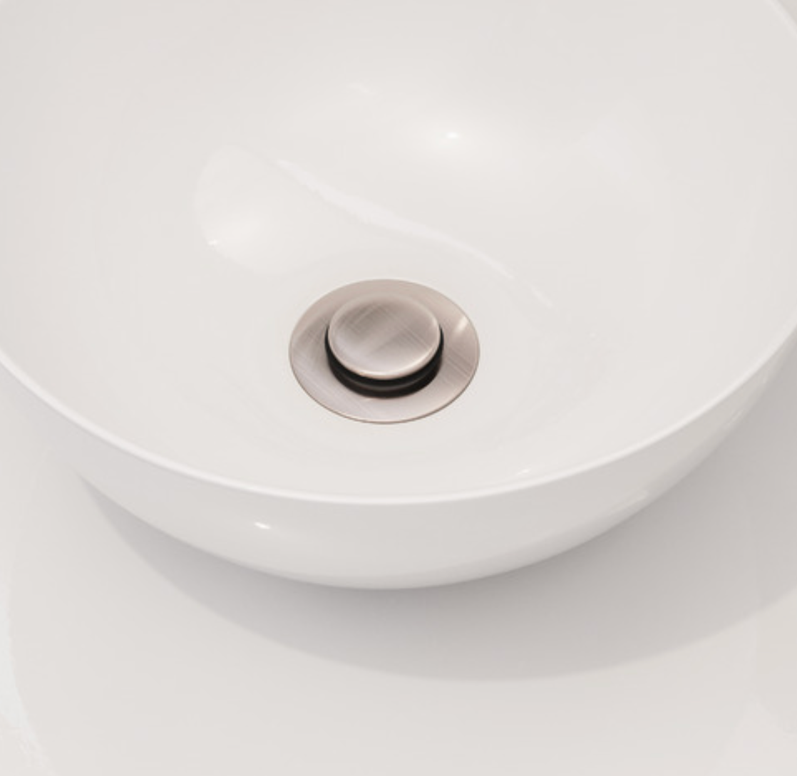 Close-up of a white ceramic sink with a silver drain cover 